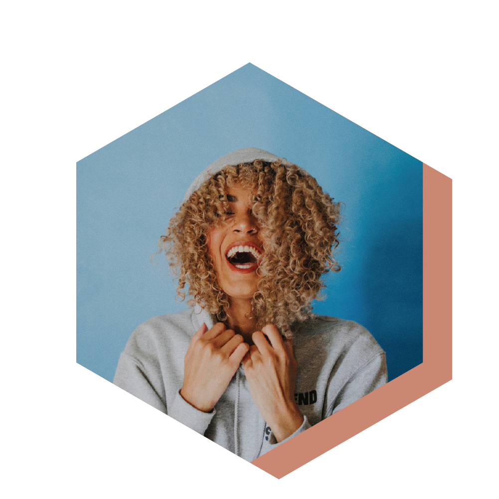 Photo of a woman with blond brown curly hear. she is smiling in a hoodie.