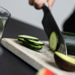 Bee Fit Coach, Shelby slicing a cucumber into round slices on a wooden cutting board.