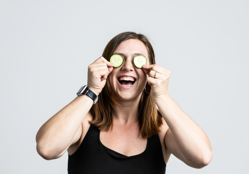 Bee Fit coach smiling and covering her eyes with sliving of cucumbers.