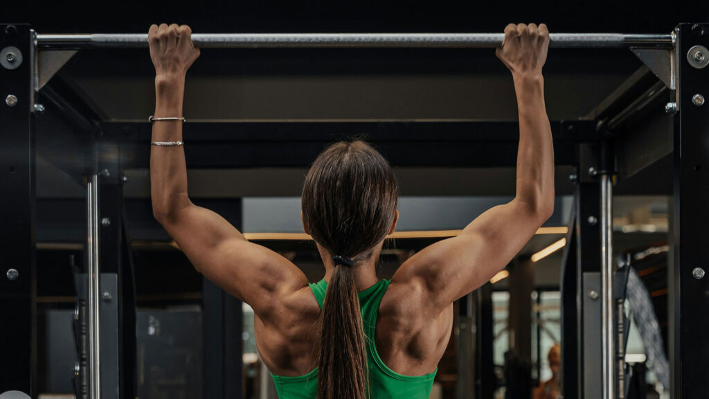 A photo of a woman doing pull-ups at the gym, she is swole. Photo by Roberto Shumski.