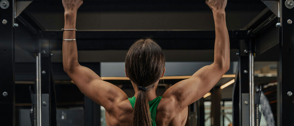 A photo of a woman doing pull-ups at the gym, she is swole. Photo by Roberto Shumski.