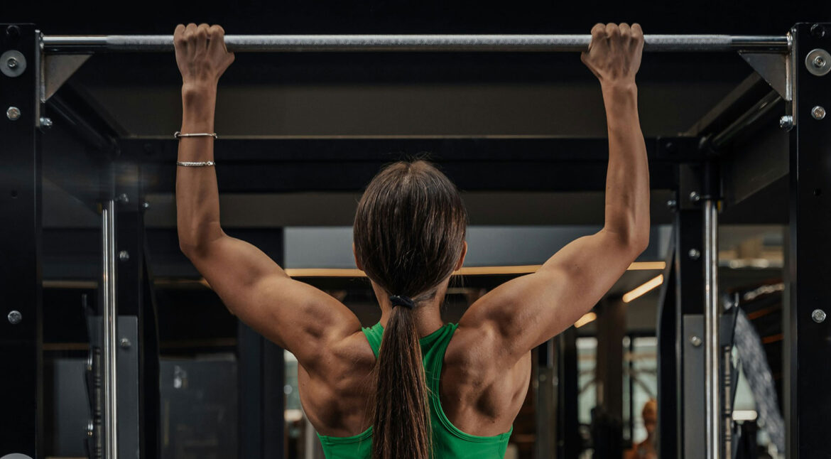 A photo of a woman doing pull-ups at the gym, she is swole. Photo by Roberto Shumski.