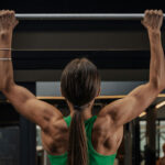 A photo of a woman doing pull-ups at the gym, she is swole. Photo by Roberto Shumski.