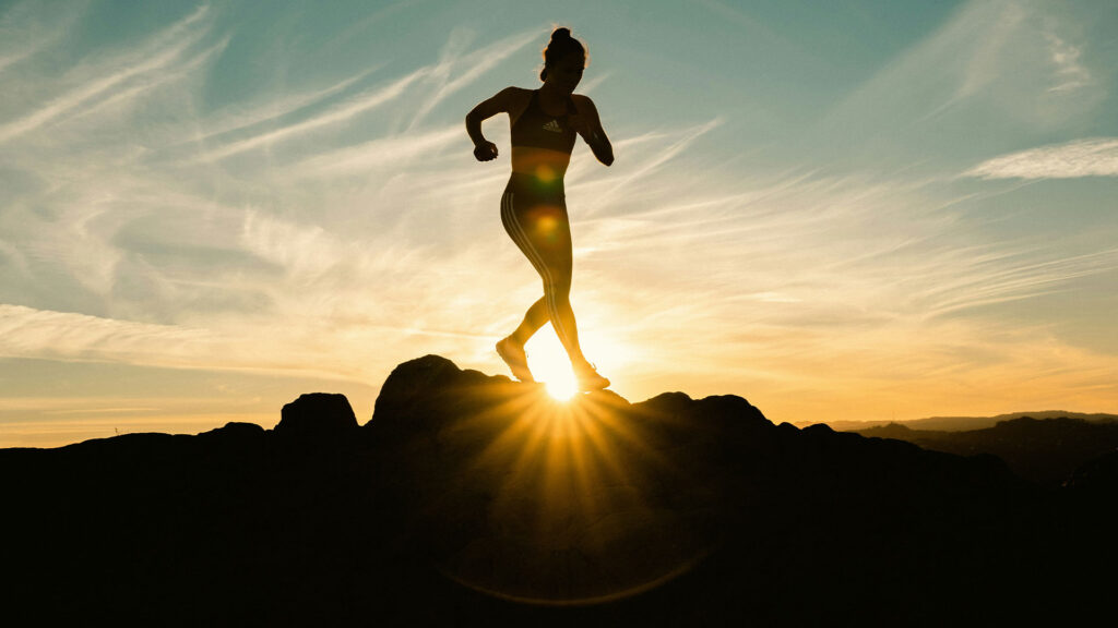 A photo of a person doing physical activity in a rocky landscape. The sun is setting behind them and they are mid-sprint. Photo by Venti Views.