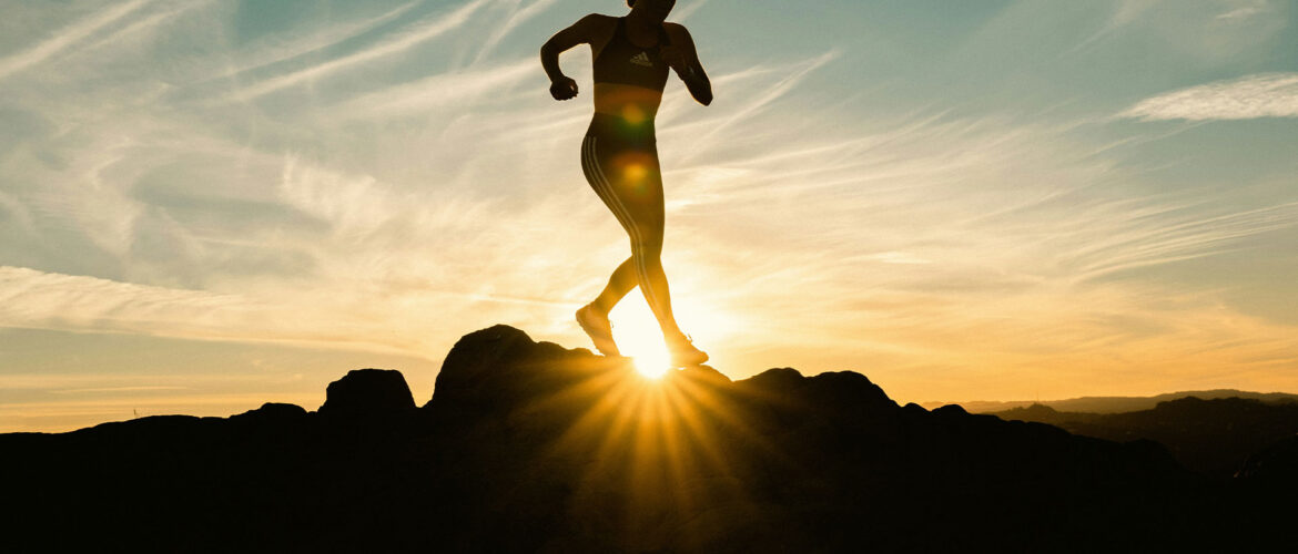 A photo of a person doing physical activity in a rocky landscape. The sun is setting behind them and they are mid-sprint. Photo by Venti Views.