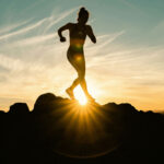 A photo of a person doing physical activity in a rocky landscape. The sun is setting behind them and they are mid-sprint. Photo by Venti Views.